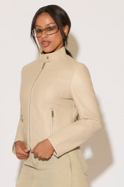 Woman wearing a nude jacket and denim skirt on a white background