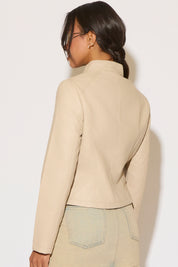 Woman wearing a nude leather jacket and denim skirt on a white background