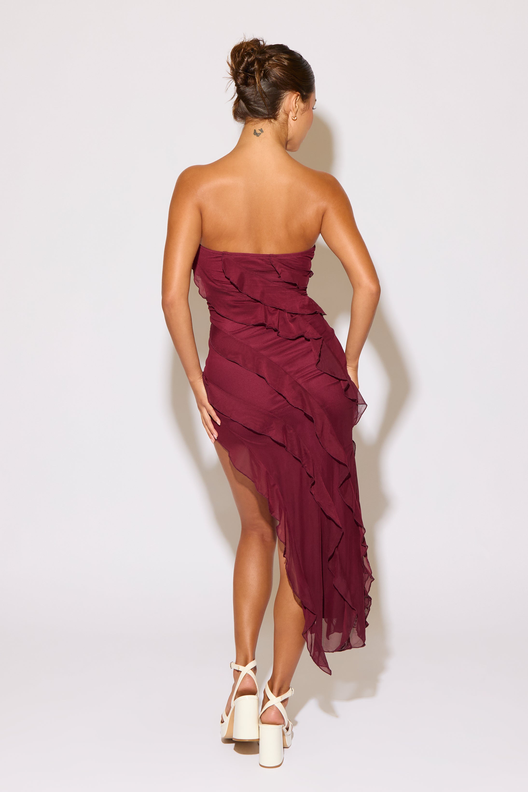 Woman wearing a strapless burgundy dress with ruffles on a white background