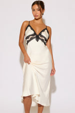 Woman wearing a white slip dress with black lace details on a plain background