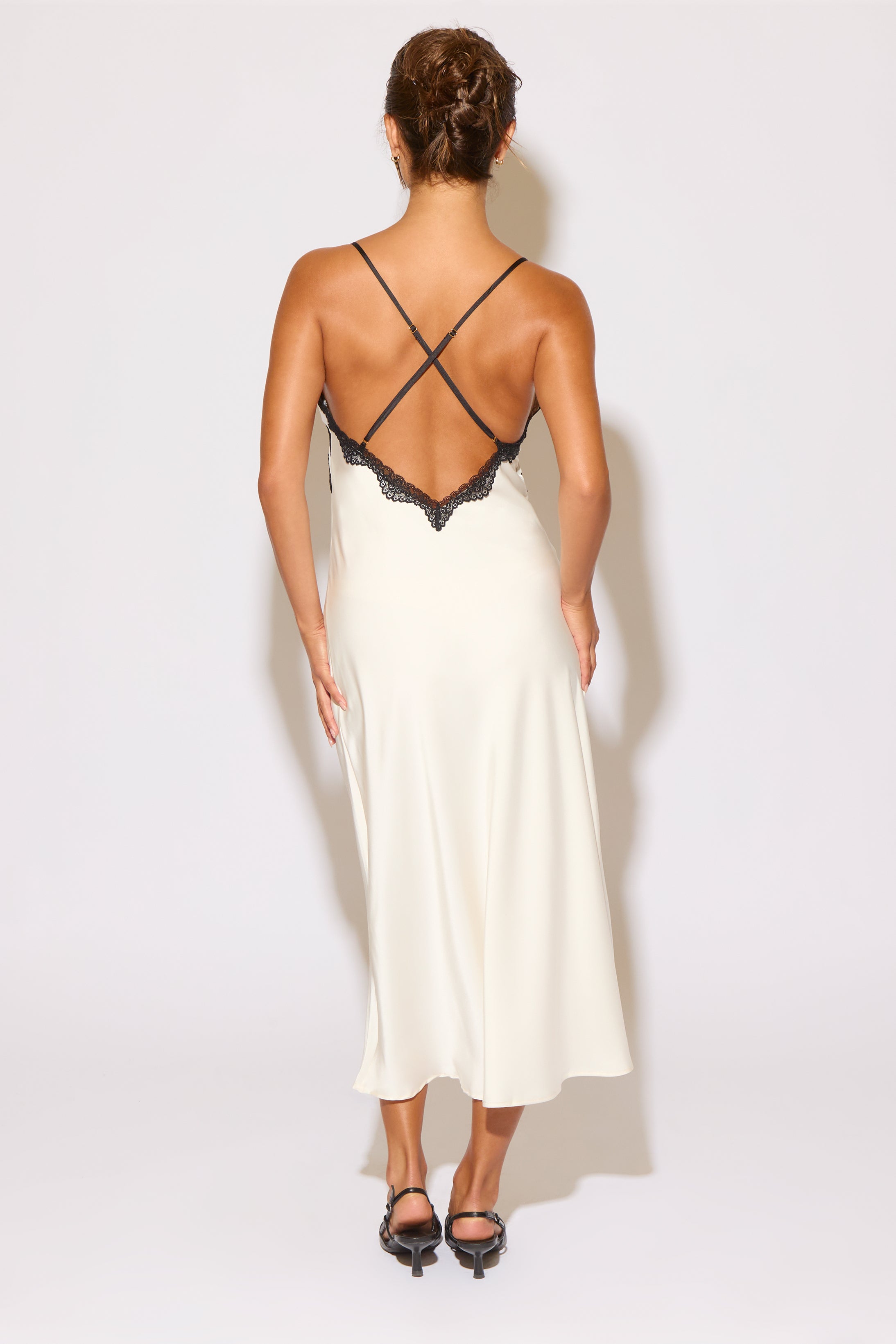 Woman wearing a white dress with black lace details on a plain background