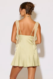 Person wearing a light green dress with thin straps against a white background