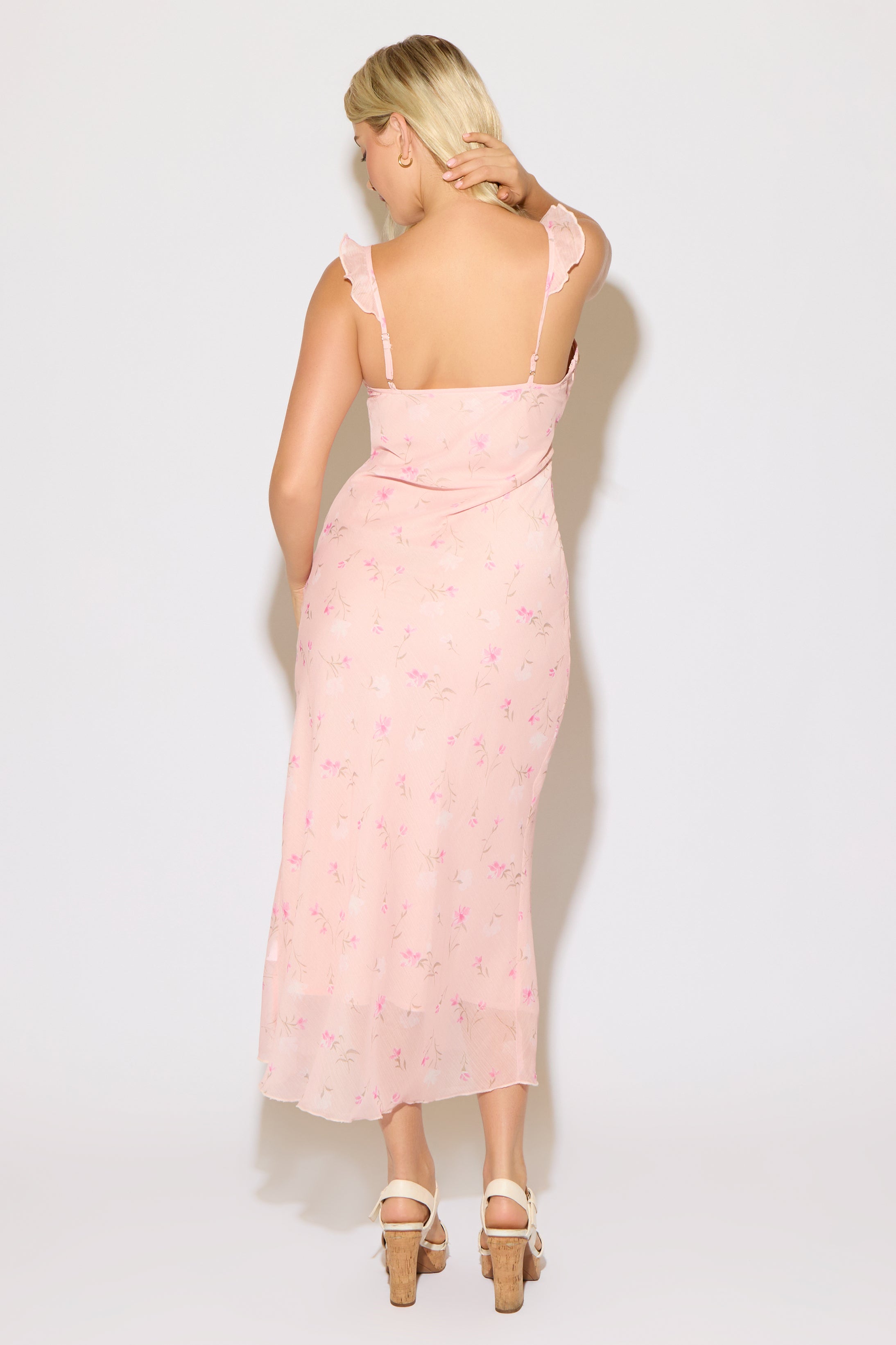 Model is wearing a pink ruffle strap v neck floral column maxi dress on a white background. 