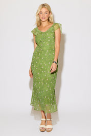Model is wearing a green mesh floral overlay dress with ruffle detail on a white background. 