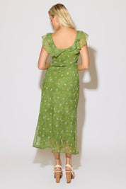 Model is wearing a green mesh floral overlay dress with ruffle detail on a white background. 