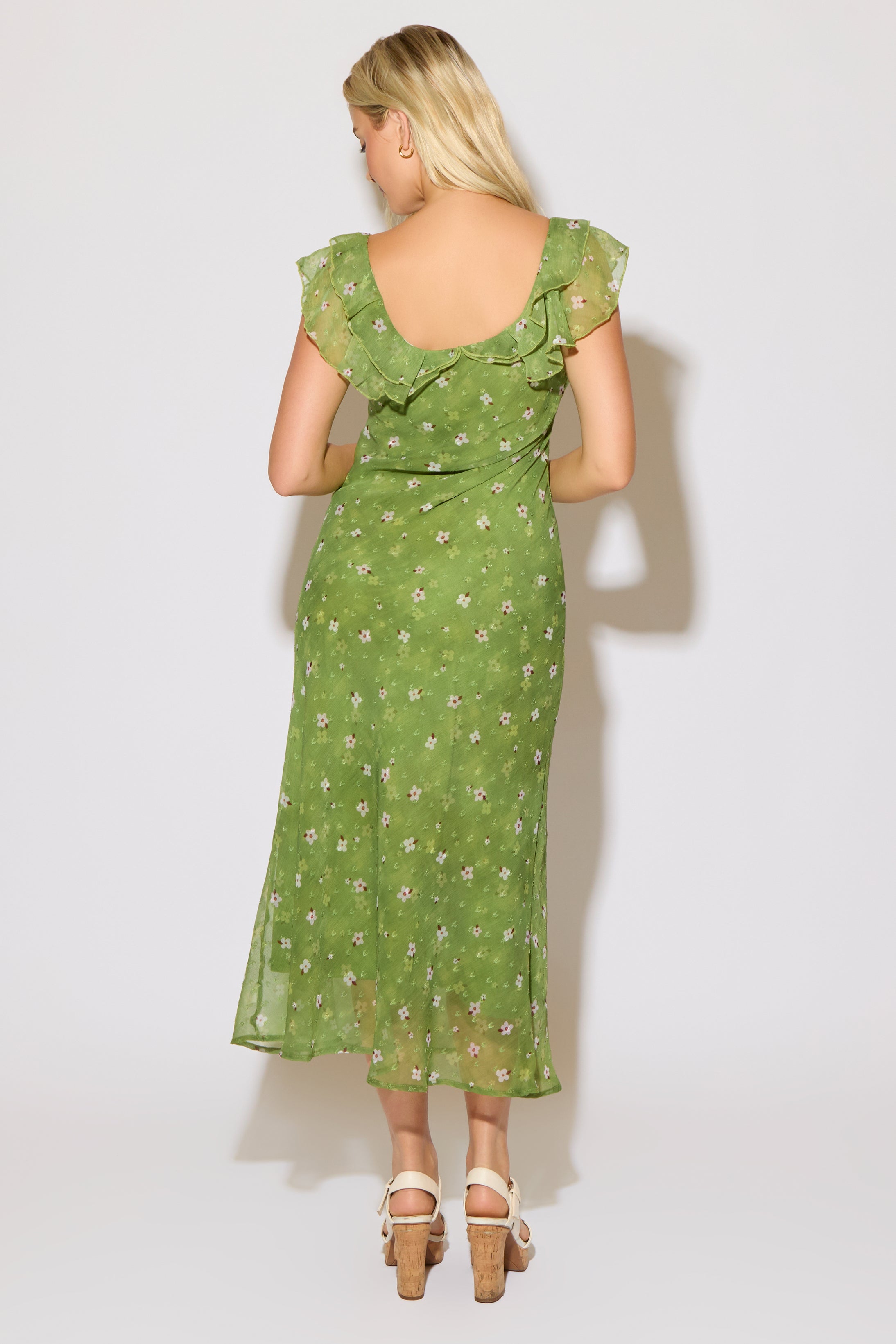 Model is wearing a green mesh floral overlay dress with ruffle detail on a white background. 