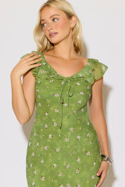 Model is wearing a green mesh floral overlay dress with ruffle detail on a white background. 