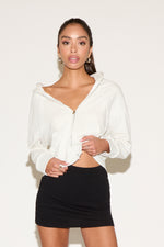Model wearing a gray zip jacket with a relaxed fit an a black mini skirt , standing against a neutral studio background.