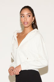 Model wearing a gray zip jacket with a relaxed fit an a black mini skirt , standing against a neutral studio background.