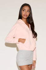 Model wearing a pink zip jacket with a relaxed fit an a gray mini skirt , standing against a neutral studio background.