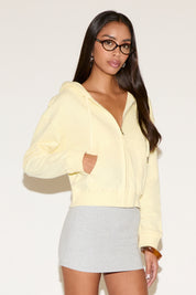 Model wearing a yellow zip jacket with a relaxed fit an a gray mini skirt , standing against a neutral studio background.
