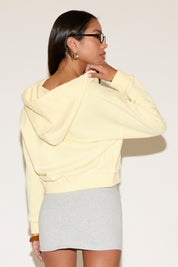 Back of model wearing a yellow zip jacket with a relaxed fit an a gray mini skirt , standing against a neutral studio background.