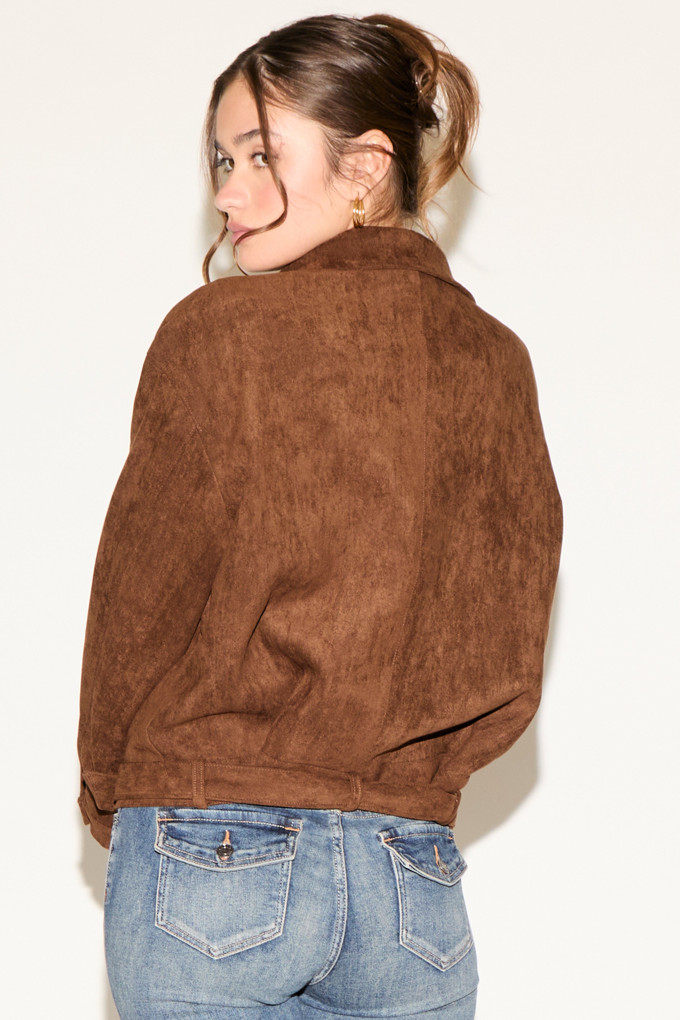 Person wearing a brown suede jacket and blue jeans against a plain background