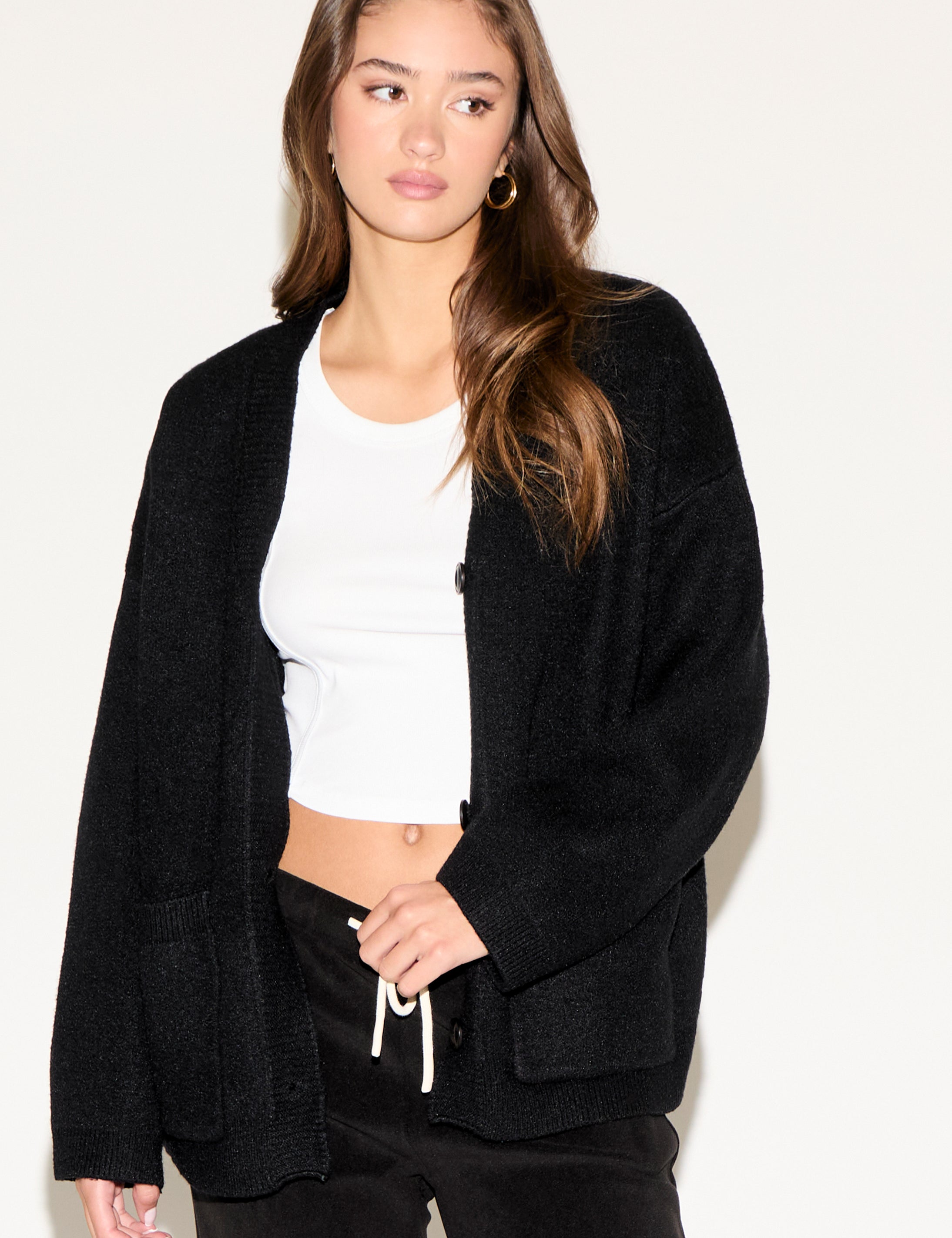 Woman wearing a black cardigan over a white top and black pants on a plain background