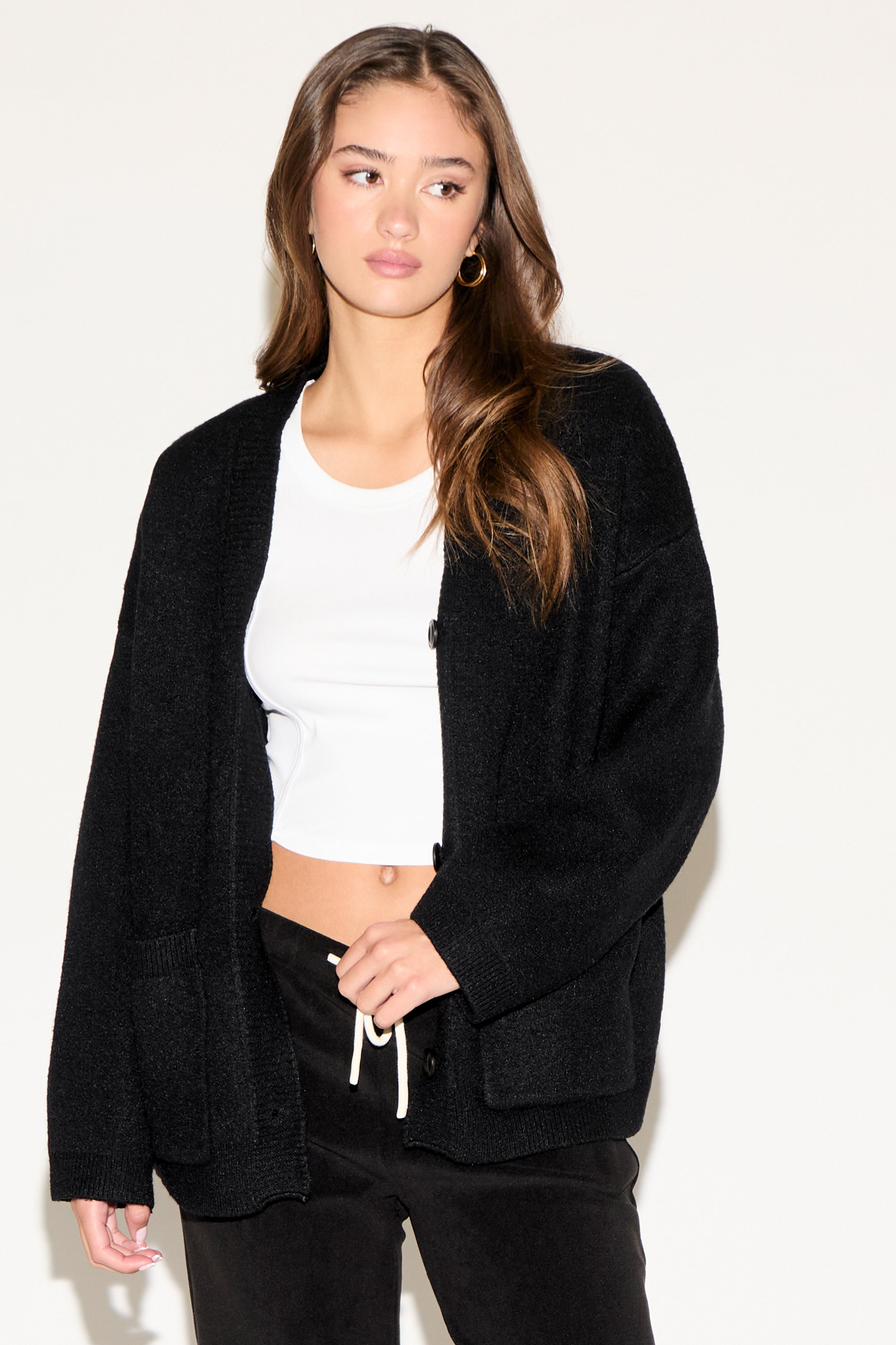 Woman wearing a black cardigan over a white top and black pants on a plain background