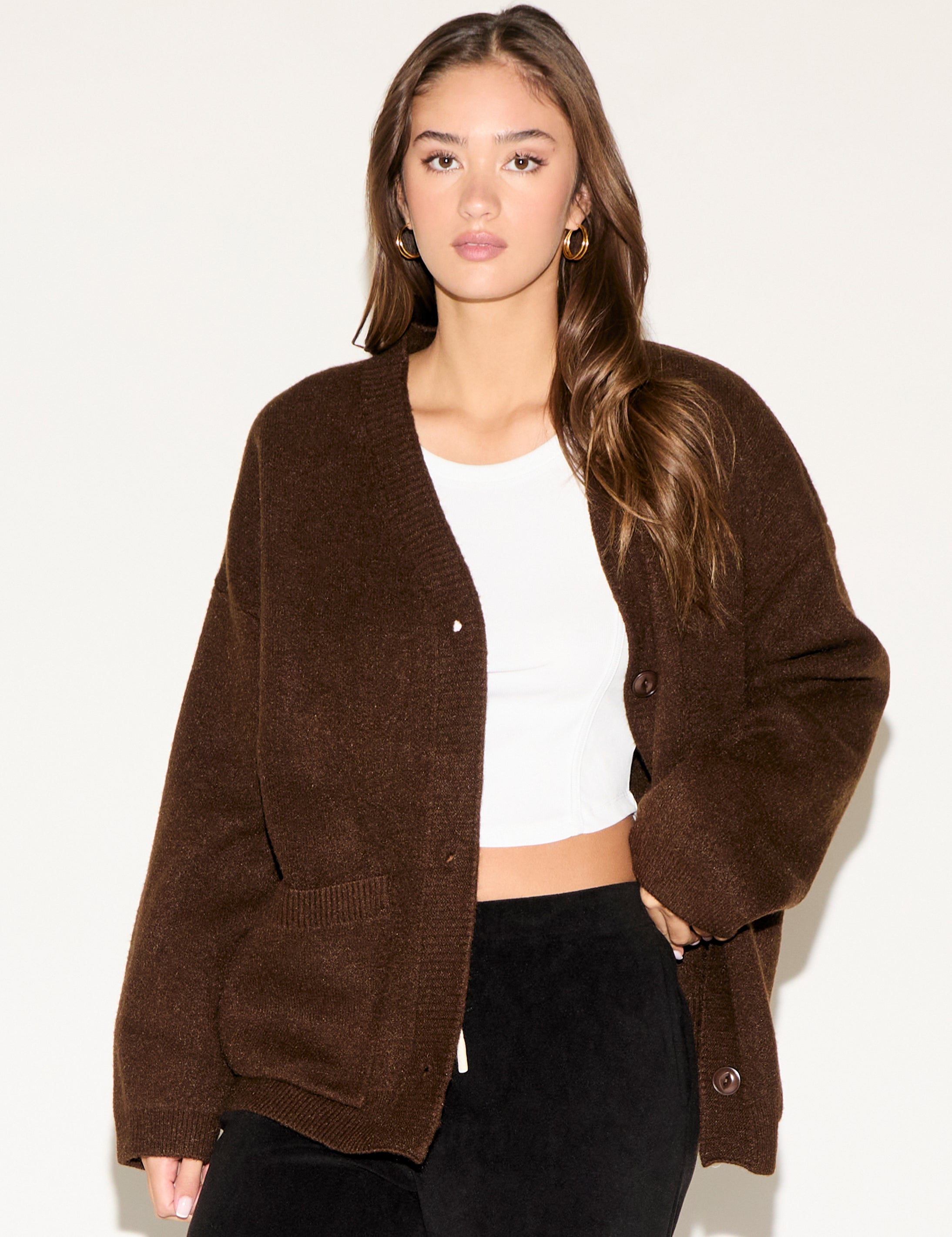 Woman wearing a brown cardigan over a white top and black pants on a white background