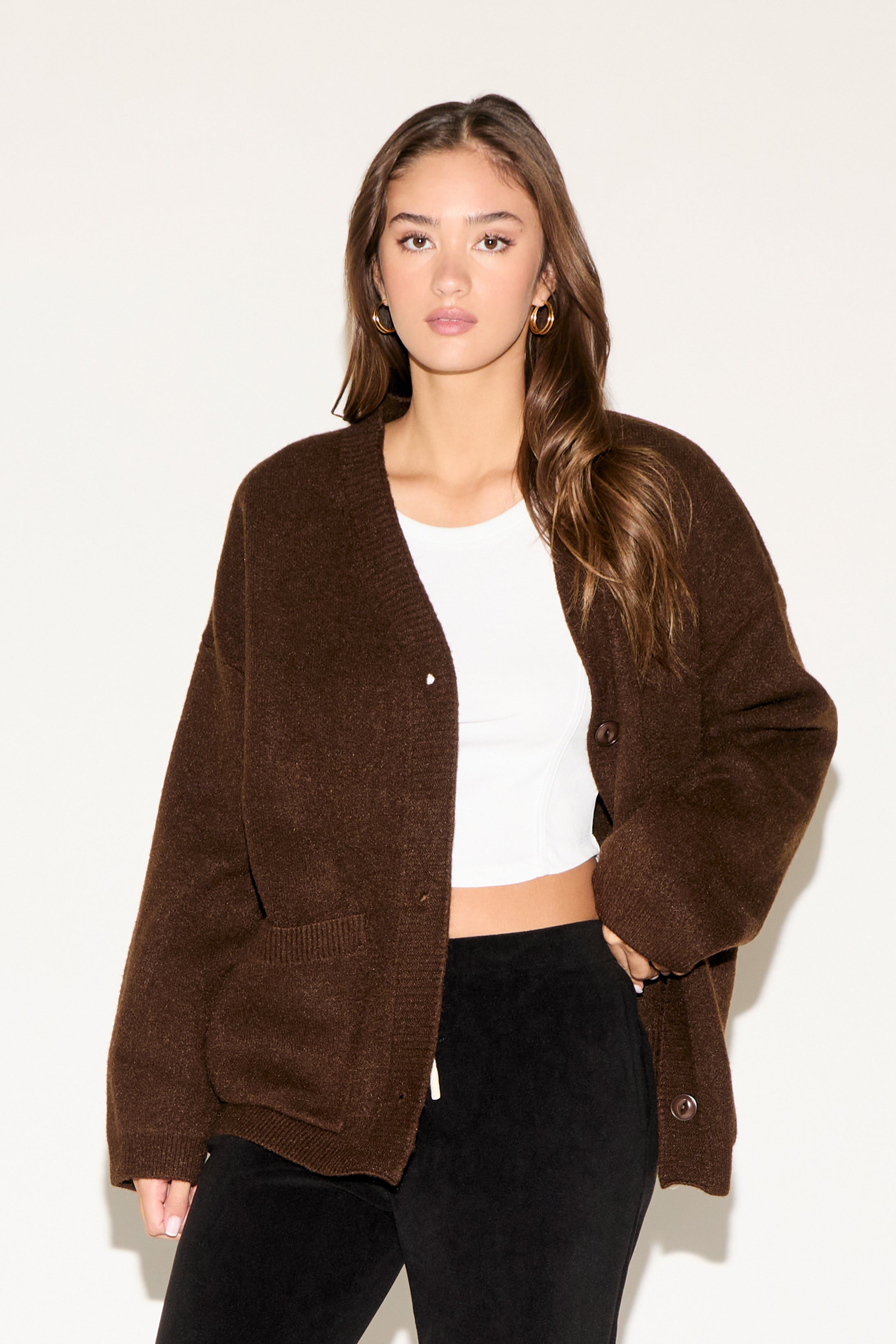 Woman wearing a brown cardigan over a white top and black pants on a white background