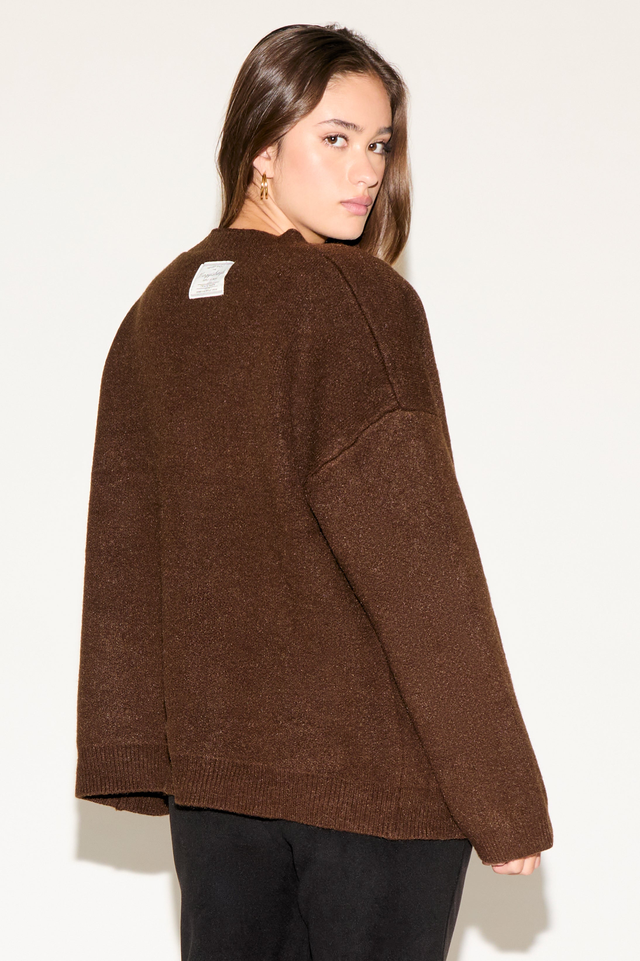 Woman wearing a brown sweater with a white square on the back against a plain background