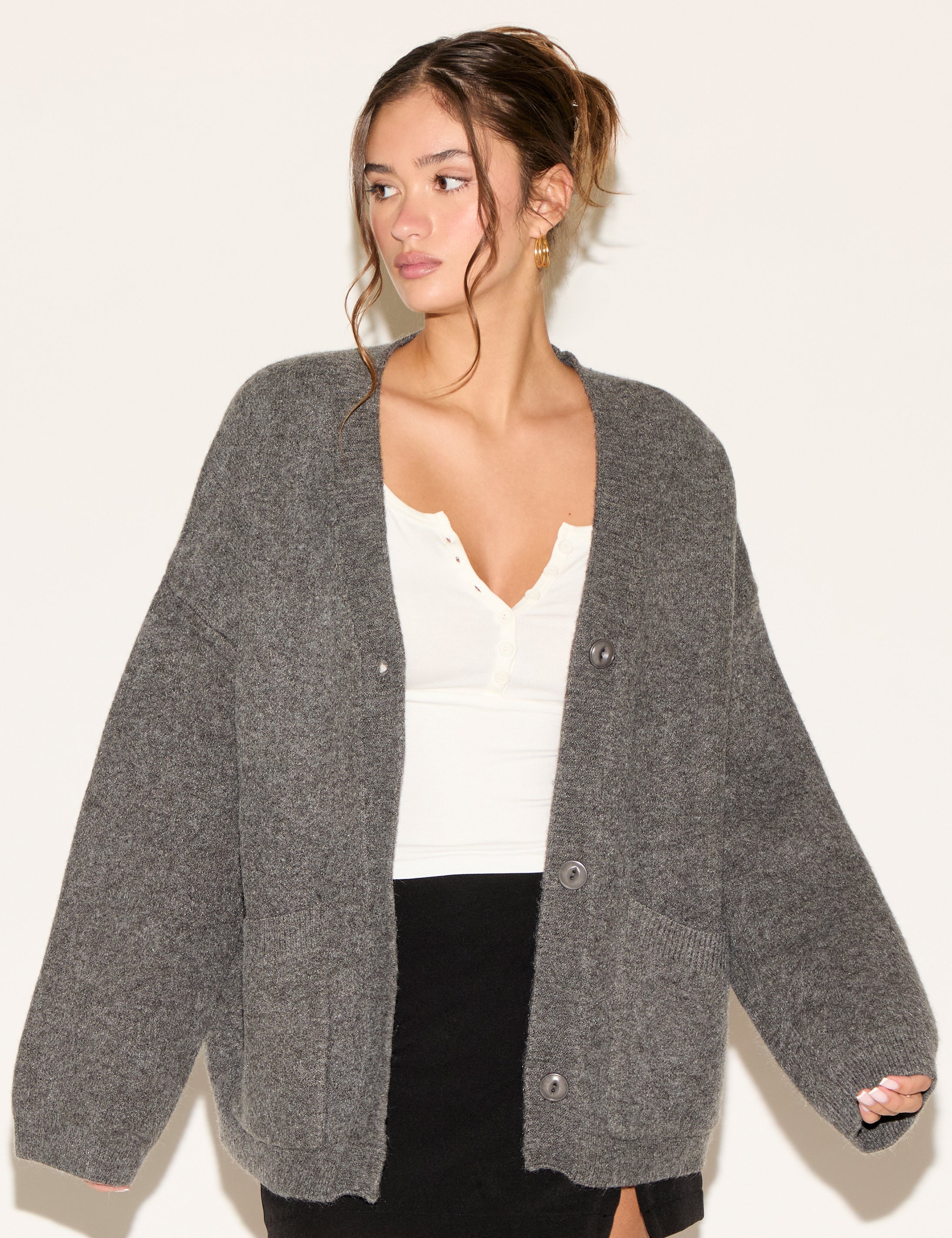 Woman wearing a gray cardigan over a white top and black skirt on a plain background