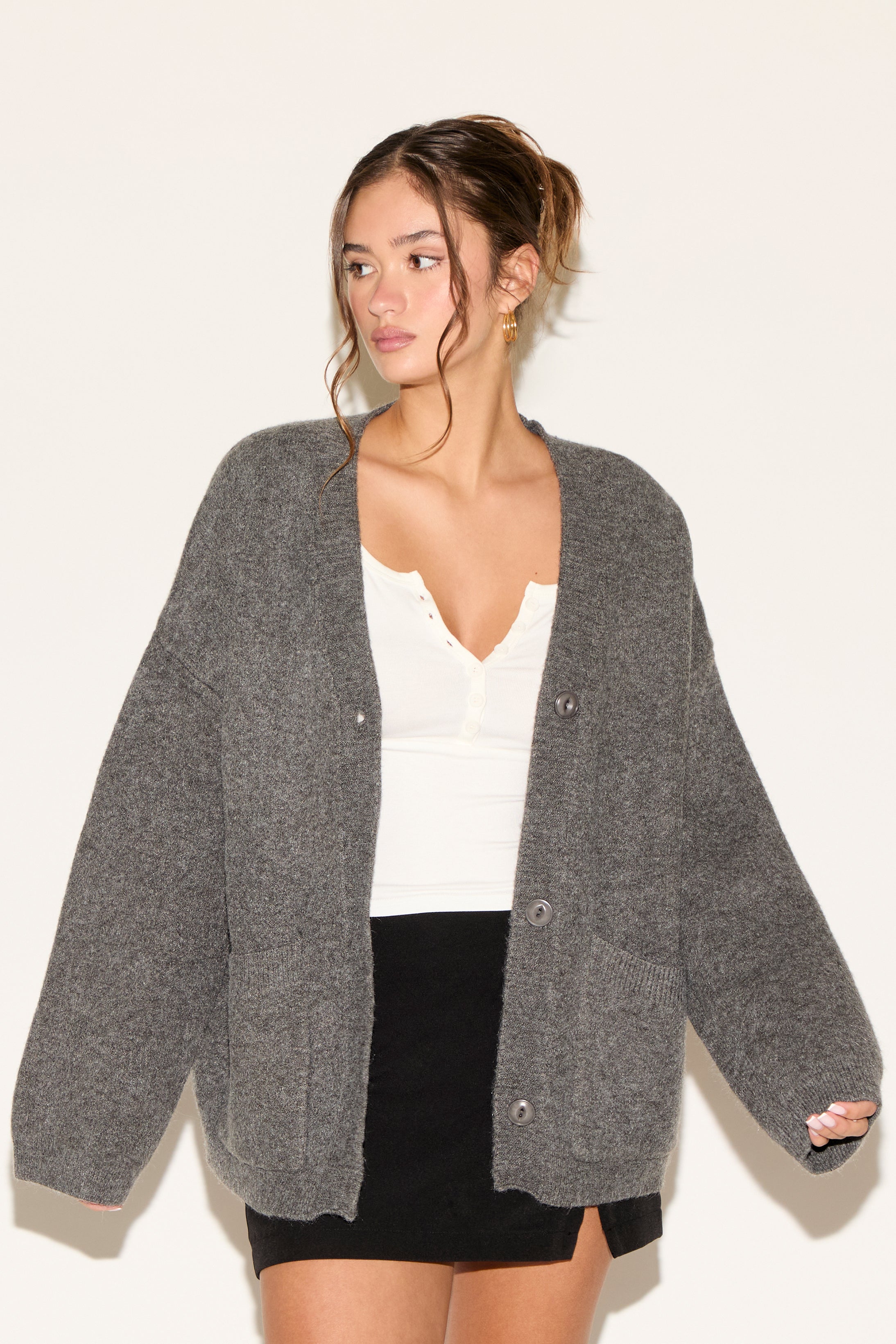 Woman wearing a gray cardigan over a white top and black skirt on a plain background