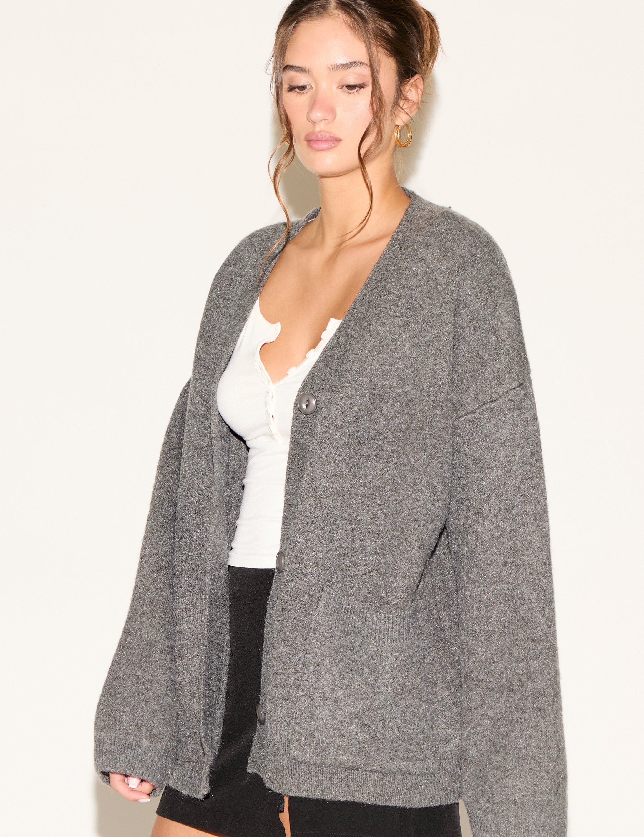 Woman wearing a gray cardigan over a white top and black shorts on a plain background