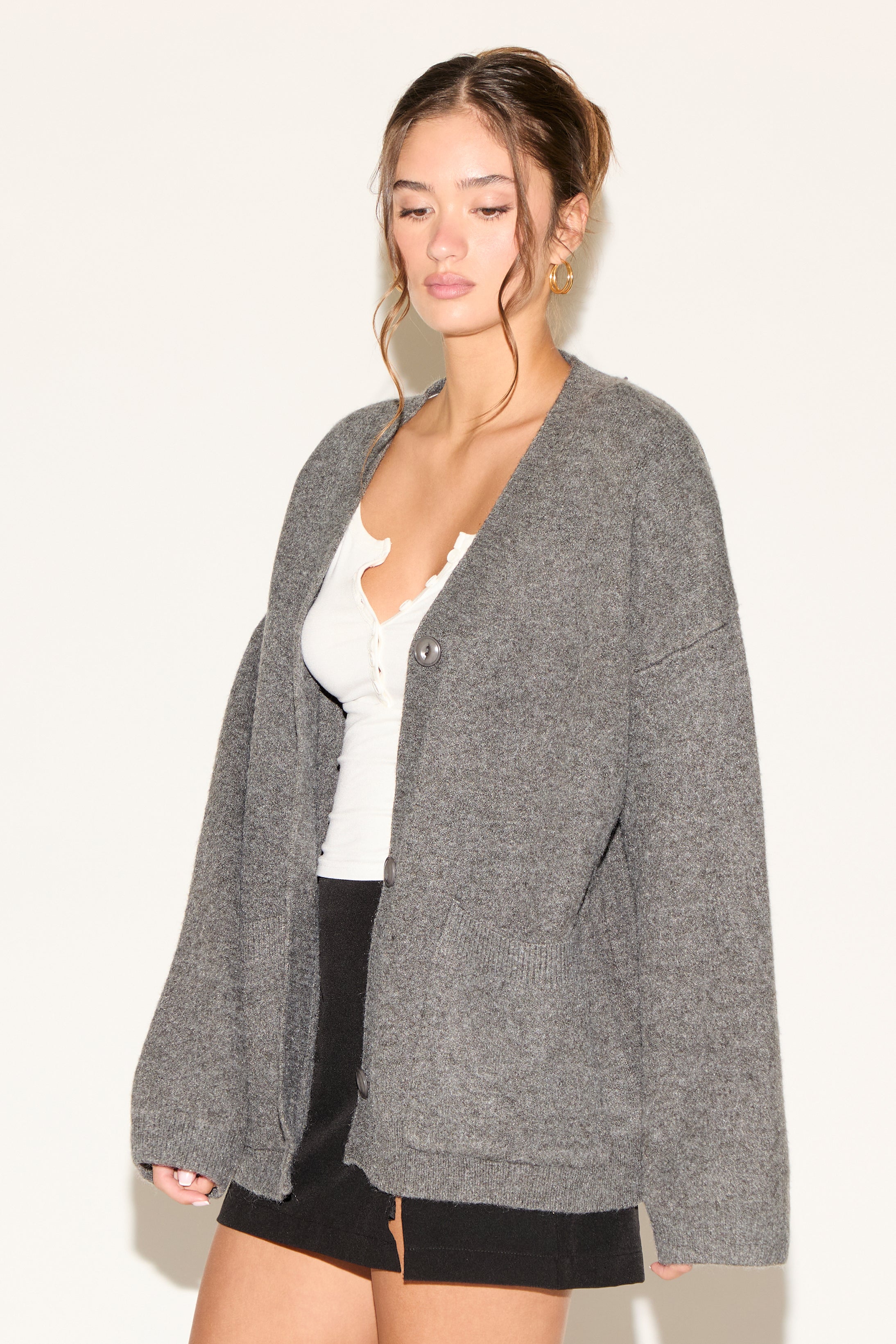 Woman wearing a gray cardigan over a white top and black shorts on a plain background