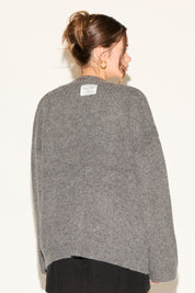 Person wearing a gray sweater with a visible brand label on a white background