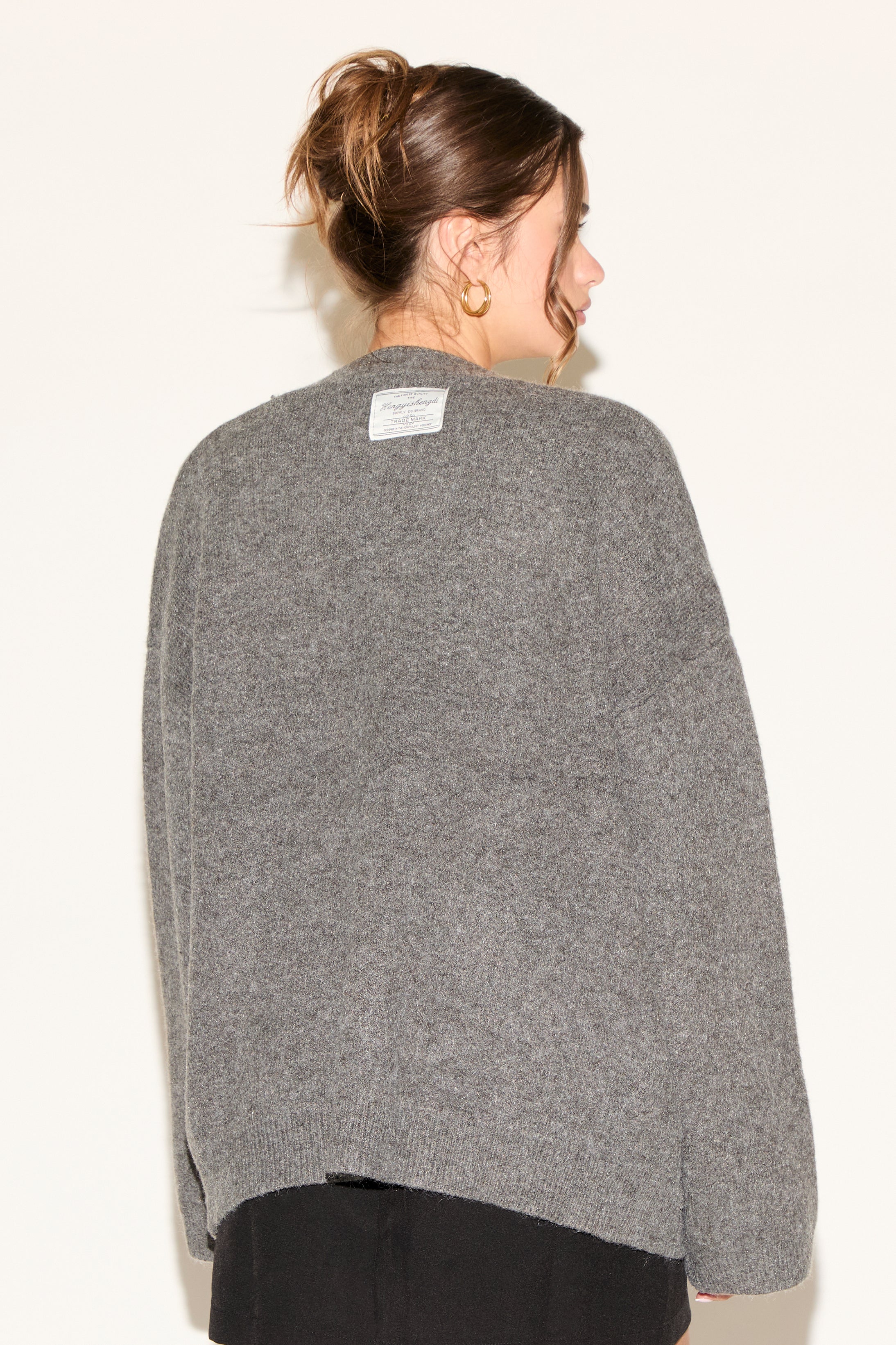 Person wearing a gray sweater with a visible brand label on a white background