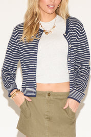 A woman wearing a navy striped cardigan over a white crop top and olive skirt. 