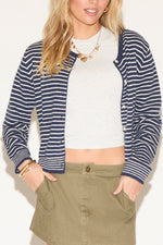 A woman wearing a navy striped cardigan over a white crop top and olive skirt. 