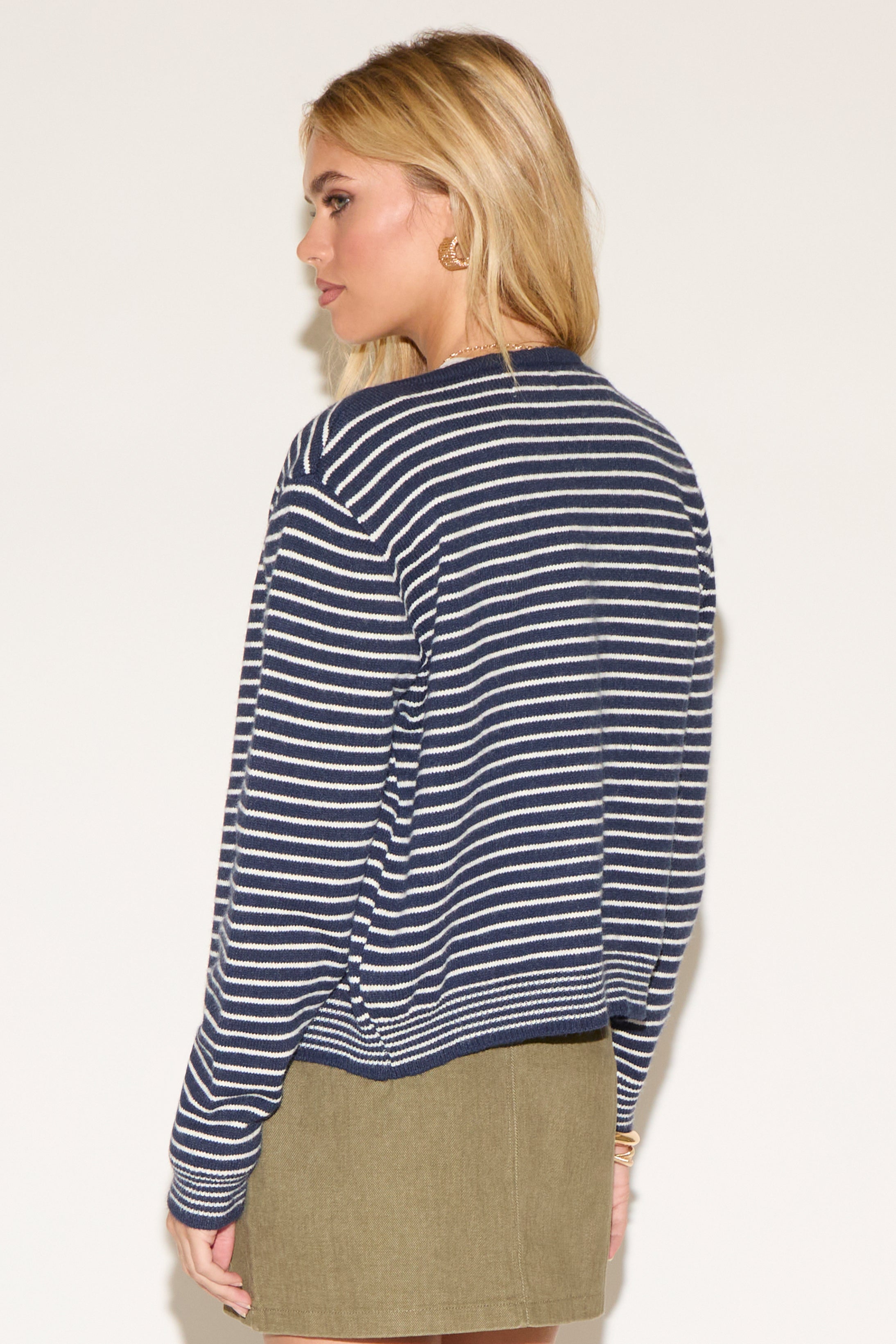 A woman wearing a navy striped cardigan over a white crop top and olive skirt. 