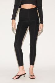 Person in black high-waisted leggings and a cropped long-sleeve top, wearing black heeled sandals, standing against a plain white background.