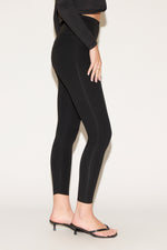 Person in black high-waisted leggings and a cropped long-sleeve top, wearing black heeled sandals, standing against a plain white background.
