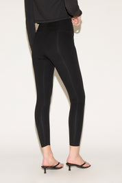 Person in black high-waisted leggings and a cropped long-sleeve top, wearing black heeled sandals, standing against a plain white background.