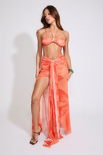 Model is wearing a orange LILY PRINT HALTER BRA TOP & WATERFALL MAXI SKIRT SET with brown heels on a white background.