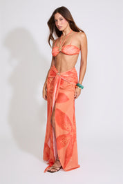 Model is wearing a orange LILY PRINT HALTER BRA TOP & WATERFALL MAXI SKIRT SET with brown heels on a white background.