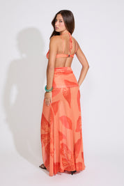 Model is wearing a orange LILY PRINT HALTER BRA TOP & WATERFALL MAXI SKIRT SET with brown heels on a white background.