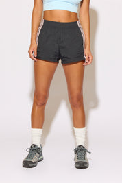 Person wearing black shorts with white stripes on a plain background