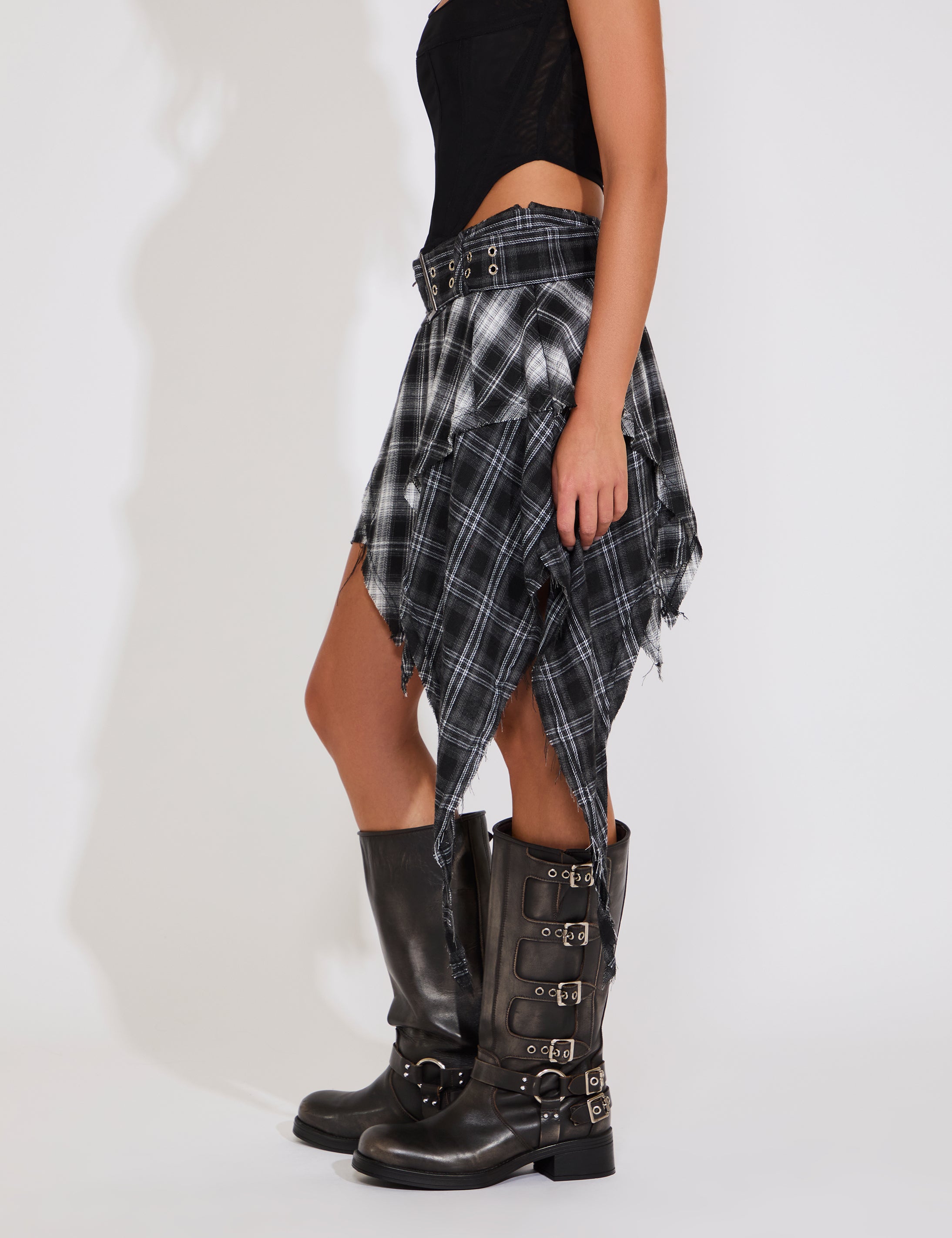 Person wearing a black and white plaid skirt with high boots on a white background