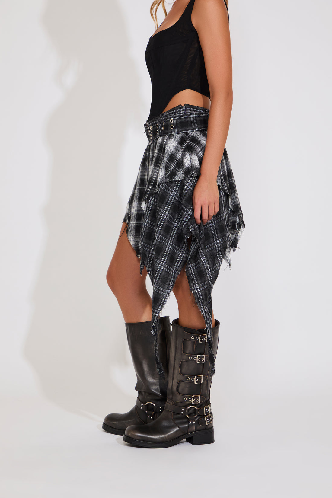 Person wearing a black tank top, plaid skirt, and black knee-high boots on a white background