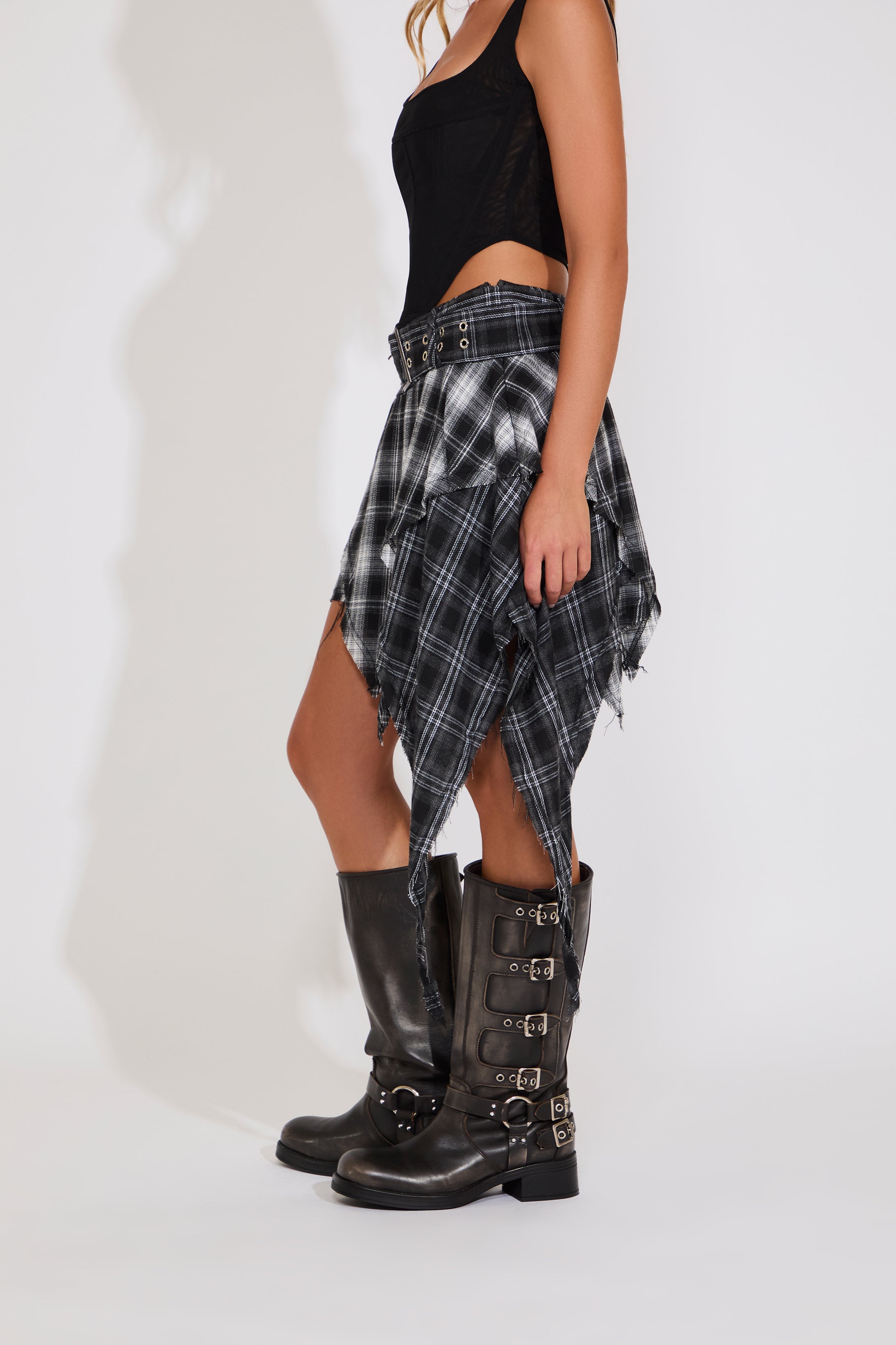 Person wearing a black and white plaid skirt with high boots on a white background