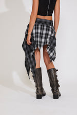 Person wearing a black and white plaid skirt with brown boots on a white background