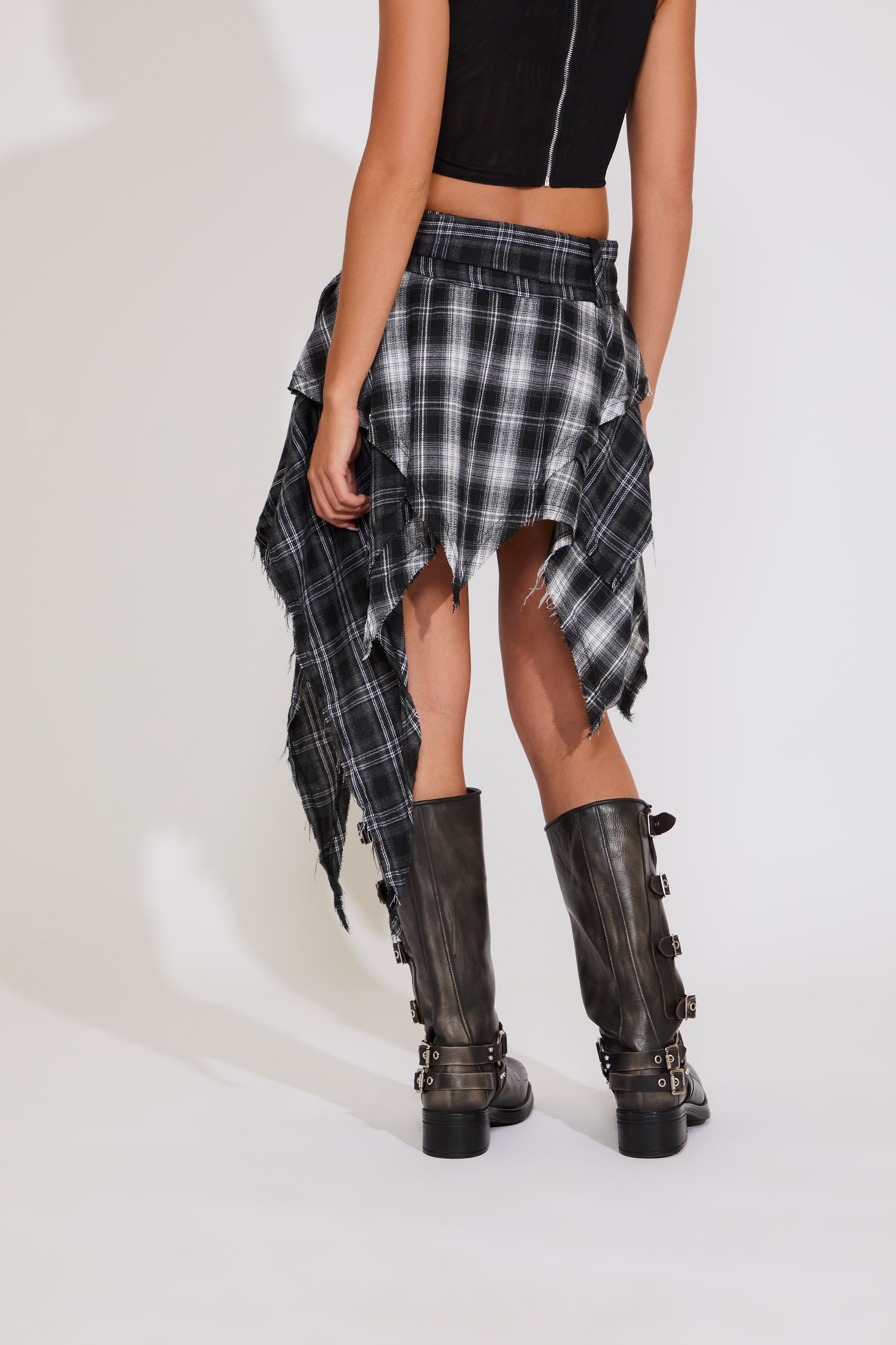 Person wearing a black and white plaid skirt with brown boots on a white background