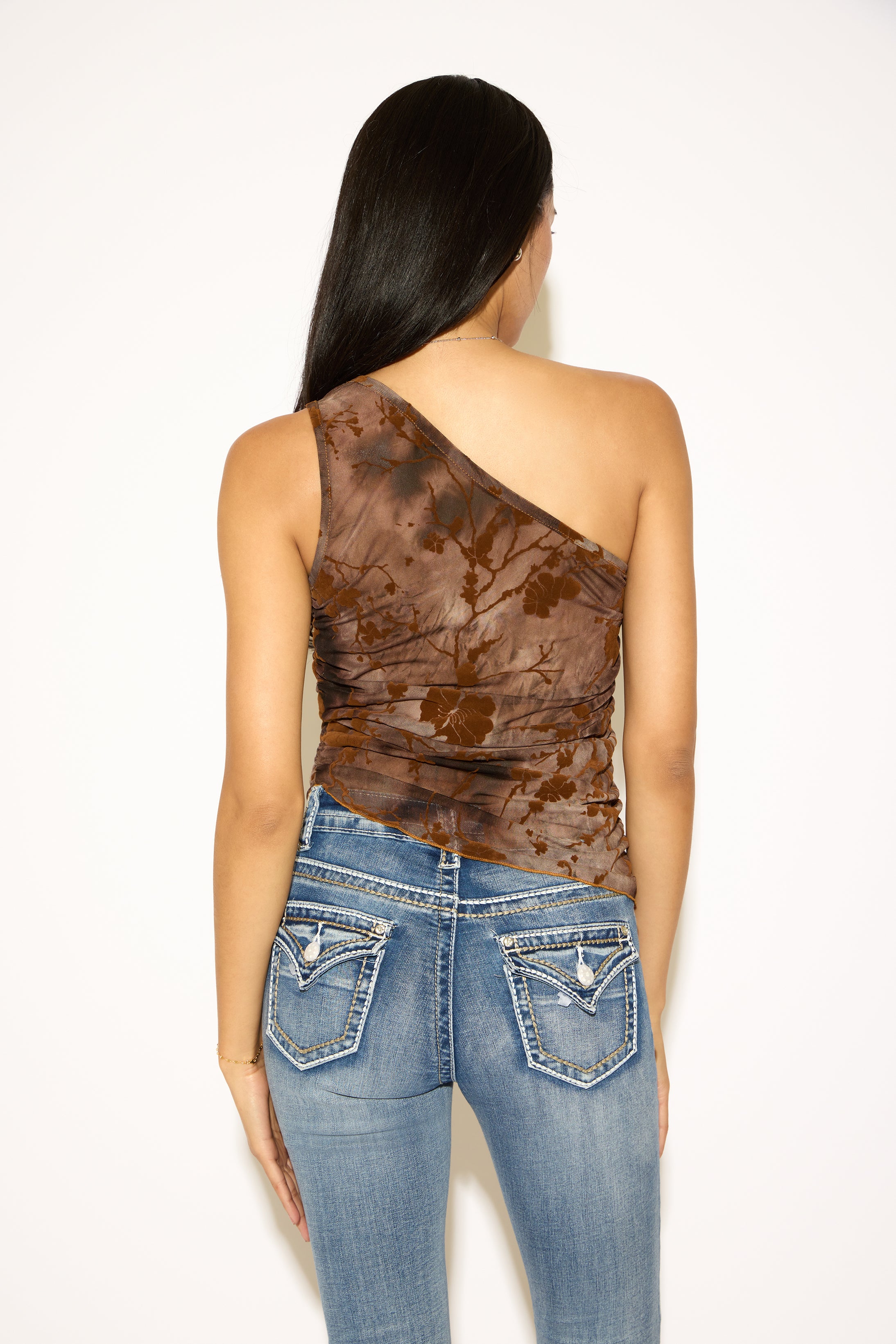 Woman wearing a brown one-shoulder top and blue jeans on a white background