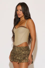 Woman wearing a beige corset top and camouflage shorts against a white background