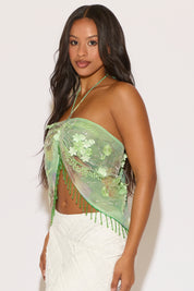 Woman wearing a green embroidered halter top with white pants on a plain background