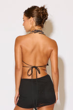 Woman wearing a black halter top and shorts with a plain background