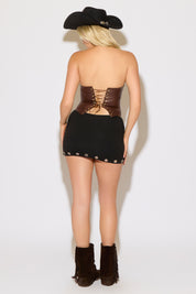 Model is wearing a brown zip front vegan leather strapless corset top with a black skirt on a white background.
