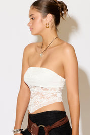 Woman wearing a white lace strapless top against a plain background