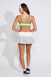 Model is wearing a green a yellow Brazil logo bralette top with a heather grey hoodie and a heather grey pleated skirts on a white background.